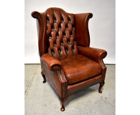 A reproduction dark tan leather button pressed and stud decorated wingback armchair, raised on cabriole supports to pad feet.