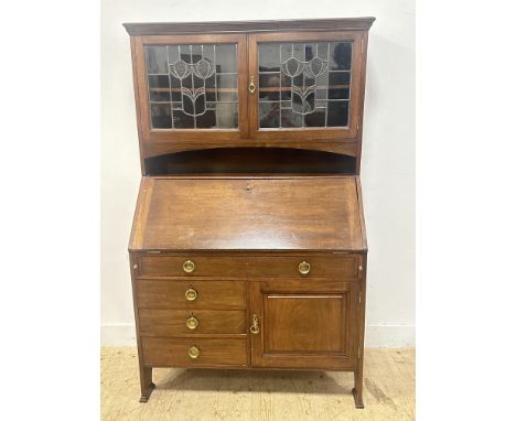 An Edwardian dark stained oak Arts &amp; Crafts Liberty style bureau cabinet, with leaded glass doors to top and fall front, 