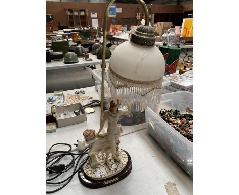 A LAMP WITH A CERAMIC FIGURE OF A LADY LEANING ON A BENCH WITH FLOWERS WITH A GLASS FRINGED SHADE 