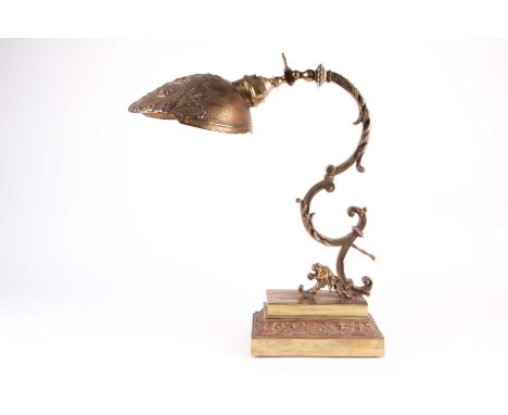 A Norman Perry gilt brass desk lamp, 20th century, with scrolled arm and shade formed as a stylised military helmet, the rear