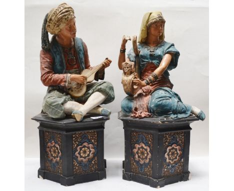 Pair of Gesetz Geschutzt Autrian polychrome painted pottery figures, modelled as a seated Arabic gentleman playing a stringed