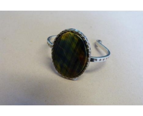 A modern silver and polished stone bangle, the polished stone, displaying multi-colours, centrally set to a scalloped surroun