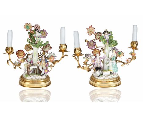 formed from curved gilt bases, the porcelain moulded as a naturalistic base with applied flowers and foliage with gilt-edging