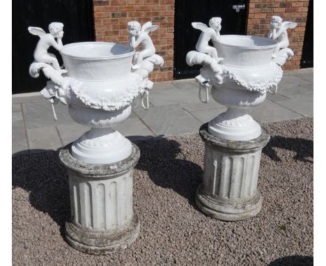 Two large painted bronze urns depicting cherubs on reconstituted stone plinths - Height: 158cm 