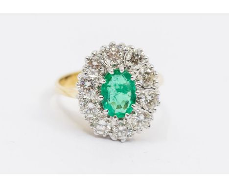 An emerald and diamond cluster 18ct gold ring, comprising an oval emerald set to the centre, approx 6 x 8mm, within a border 