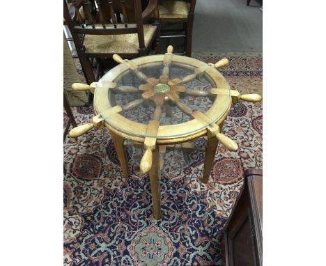 A light wood side table in the form of a ships wheel with a glass top