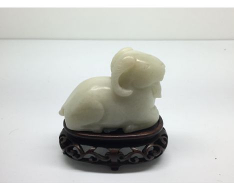 A small, carved white jade model of a seated ram on carved wooden stand.Approx 6cm long