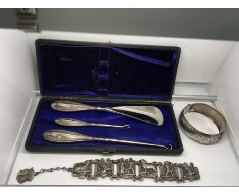 A cased silver boot hook set, an engraved silver bangle and white metal bracelet set with Egyptian motifs