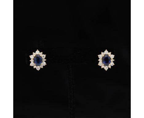 14k yellow gold earrings each set with oval cut central sapphire and surrounded by alternating larger and smaller round brill