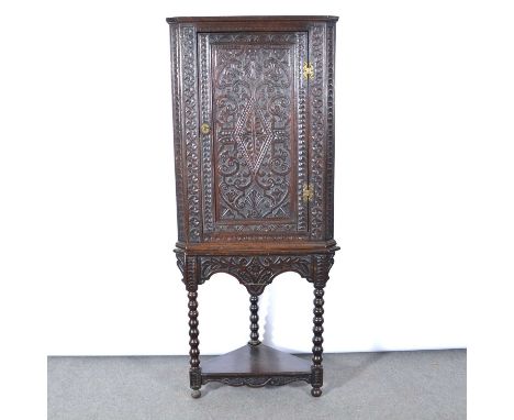 Carved oak corner cupboard, panelled door enclosing two shelves, on a related stand, bobbin-turned upright, shelf base, width