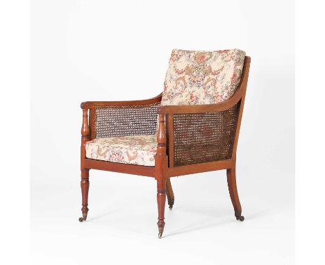 A Regency mahogany bergère library chair, a reeded frame with open column arms, with seat and back cushions, on turned legs a