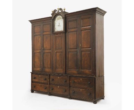 A grained oak clock cupboard, early 19th century, Shropshire, the panelled housekeeper's cupboard with a clock to the centre,