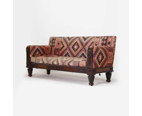 A William IV mahogany-framed sofa, the show wood with floral garland carved decoration, upholstered in kilim carpet, on turne