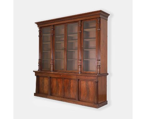 A William IV mahogany library bookcase, c.1830, with lappet-moulded and fluted columns, blind frieze drawers, and on a plinth