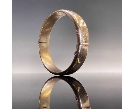 A 9ct gold hinged hollow bangle with foliate engraved decoration, stamped 375, weight 18.64g.From the Estate of Julia &amp; S