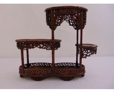 A Chinese hard wood three tier display stand of oval form on six pierced bracket feet