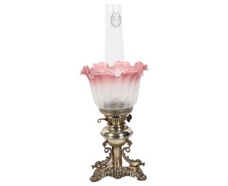 An ornate oil lamp, with an etched clear and cranberry glass frilled shade, sitting on a silver plated triangular base with s