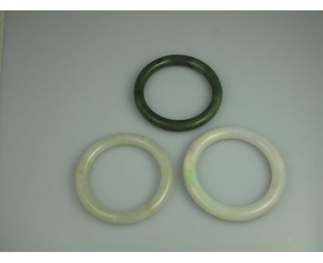 TWO POLISHED PALE GREEN JADE BANGLES AND A SPINACH JADE BANGLE.  8cm, 7.5cm and 7.5cm diameter.  Inner diameter 60mm, 57mm an