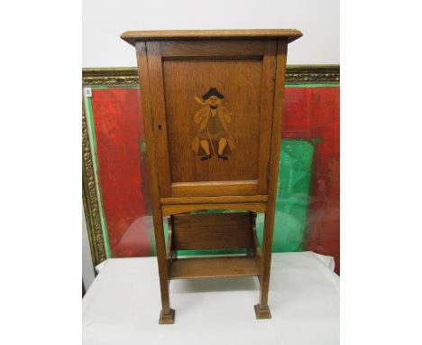 An Arts & Crafts oak and marquetry smokers cabinet, the panelled door decorated with a seated man smoking a pipe, enclosing a