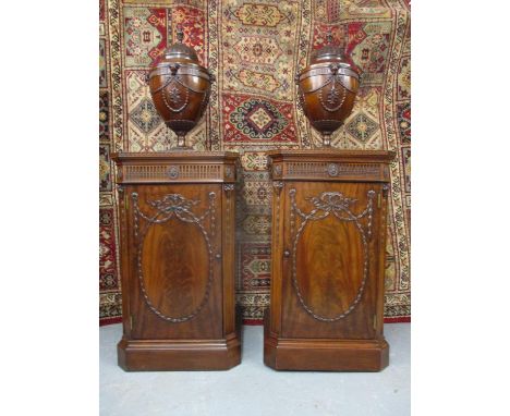 A pair of 1920s mahogany pedestals with canted front corners, a fluted and bead frieze and a door with garlands and ribbon or