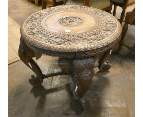 An Indian carved hardwood circular occasional table on elephant trunk legs with cross stretchers