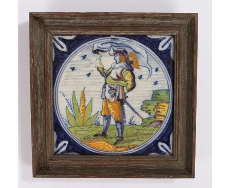 18th Century Delft tile, of a solider standing with a flag and a sword in it's hilt, housed within a frame, 17.5cm diameter i