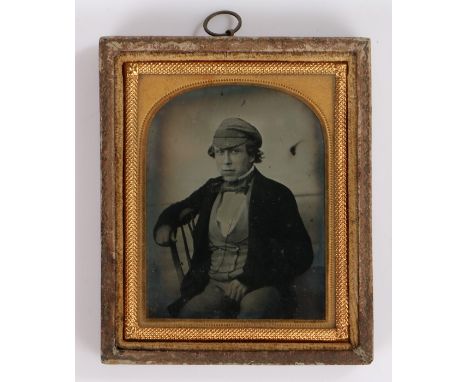 19th Century ninth plate ambrotype, of a seated man in a cap, the rear of the case with the label for SYMONS'S Photographic G