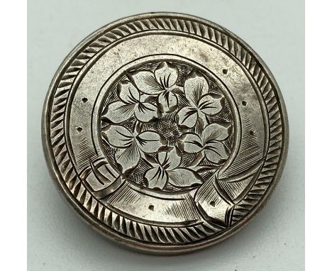 A vintage silver pin back brooch with floral detail framed with engraved belt decoration. Approx. 2.5cm diameter. 
