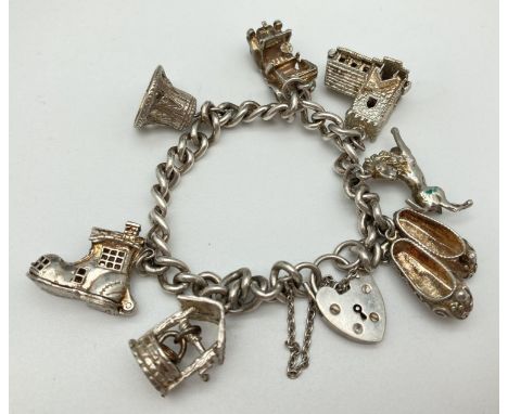 A vintage silver charm bracelet with padlock clasp, safety chain and 7 silver and white metal charms. Charms comprise: a well