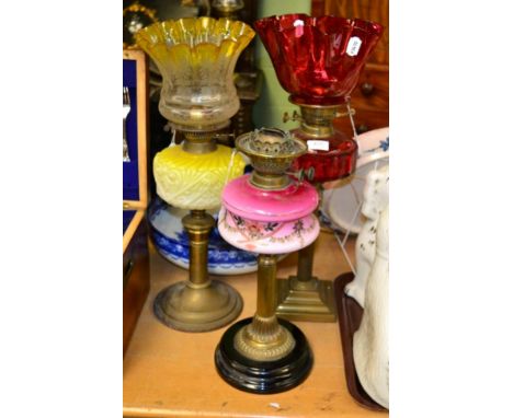 A Victorian oil lamp, cranberry shade and reservoir; together with another, yellow tinted shade and reservoir and another mis