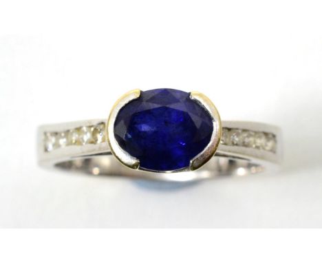 A sapphire and diamond ring, an oval cut sapphire in a half rubbed over setting, to tapering channel set diamond shoulders, t