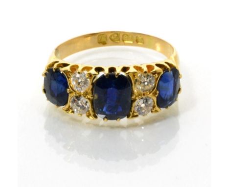 An 18 carat gold sapphire and diamond ring, three oval cut sapphires spaced by pairs of old cut diamonds, to a carved shank, 