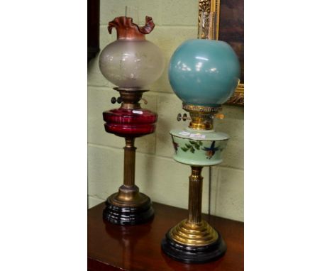 A Victorian oil lamp with cranberry glass reservoir, together with another Victorian oil lamp with a floral painted green gla
