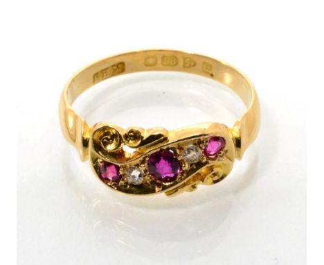 An 18 carat gold ruby and diamond ring, three graduated oval cut rubies spaced by two old cut diamonds, to a pierced scroll s