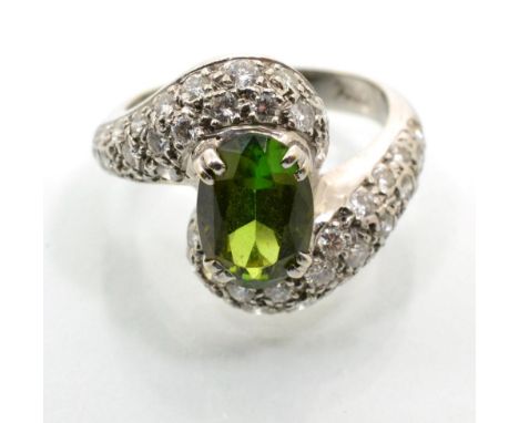 A green tourmaline and diamond twist ring, an oval cut green tourmaline in a claw setting, to pavé set diamond bypass shoulde