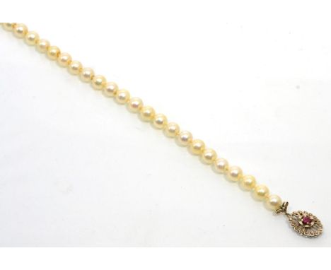 A cultured pearl necklace with an 18 carat white gold ruby set clasp, a uniform strand of cultured pearls knotted to an oval 