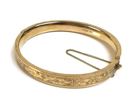 A 9ct gold bangle, with floral bright cut engraved decoration, complete with safety chain, 13.2g total weight, 58 by 49.5mm i