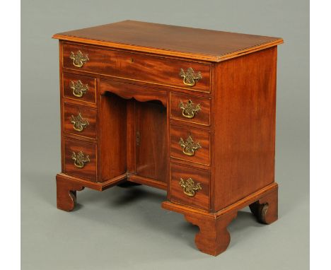 A George III mahogany kneehole desk, with applied moulded edge above a series of drawers and recessed cupboard and raised on 