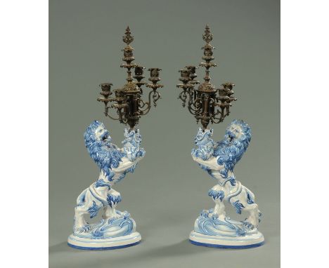 A pair of Galle tin tin glazed heraldic candelabra, late 19th century, each in the form of a rampant lion holding aloft a thi