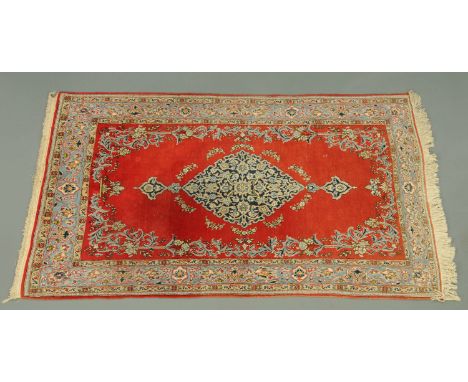 An Eastern fringed rug, circa 1970's, with centre rectangular panel in red and with multiple line border in light blues and b