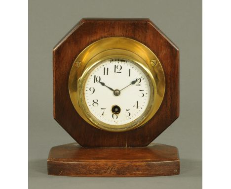 An Edwardian brass cased bulkhead clock, with single-train movement, enamel dial and raised on a wooden base.  Case diameter 