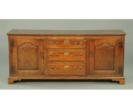 A George III oak dresser base, fitted with three centre drawers with brass drop handles and lock escutcheons, flanked on eith