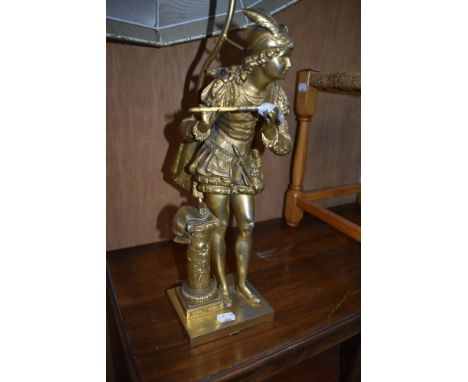 A gilt metal table lamp modelled as a piper in traditional dress, detail includes feather cap and sheet music on column stand