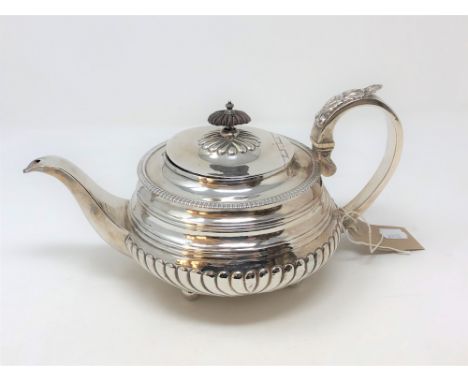 A Georgian silver teapot, maker ET, city and date marks rubbed, of gadrooned form on four ball feet, height 15cm. * Provenanc