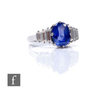 An 18ct sapphire and diamond ring, central oval claw set sapphire, length 10mm, flanked by three graduating baguette cut diam