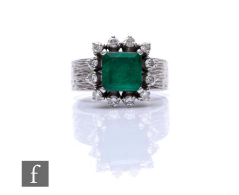 A mid 20th Century silver emerald and diamond cluster ring, square cut emerald within a border of twelve brilliant cut diamon