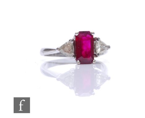 An 18ct hallmarked ruby and diamond three stone ring, central emerald cut ruby, length 9.5mm, flanked by a trillion cut diamo