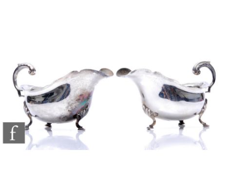 A pair of hallmarked silver sauce boats each raised on three pad feet and terminating in acanthus capped flying scroll handle