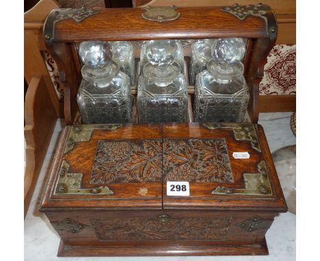 Victorian brass-bound carved oak tantalus, having three decanters and lockable compartment for glasses and games including cr