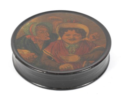 A 19th century lacquered papier mache circular snuff box. Printed with a satirical scene of an old lady grimacing and waving 